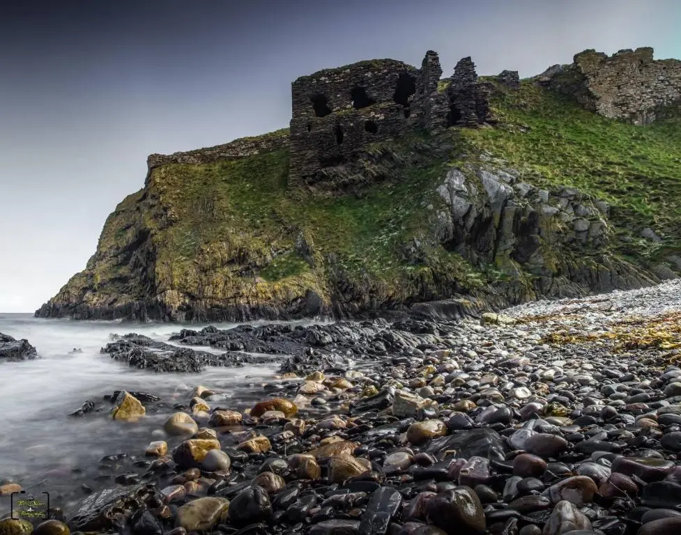 a rocky beach with a castle on the hill at Grant Arms Hotel in Cullen
