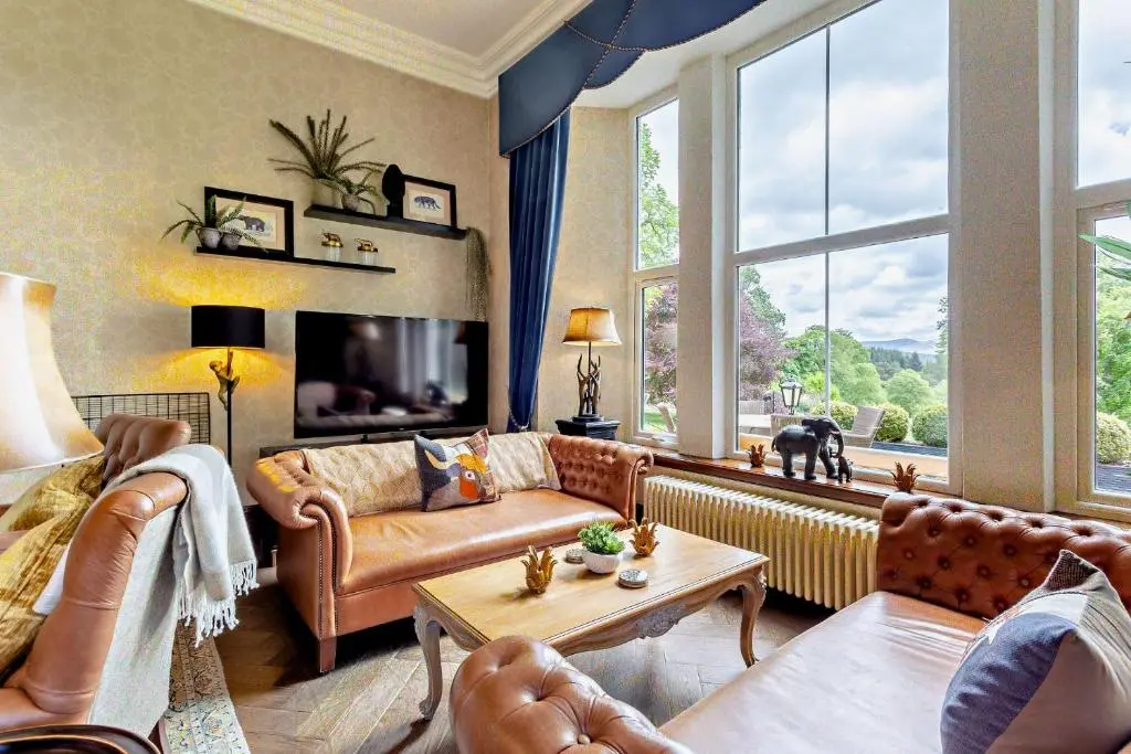 a living room with leather furniture and a large window at Muckrach Country House in Skye of Curr