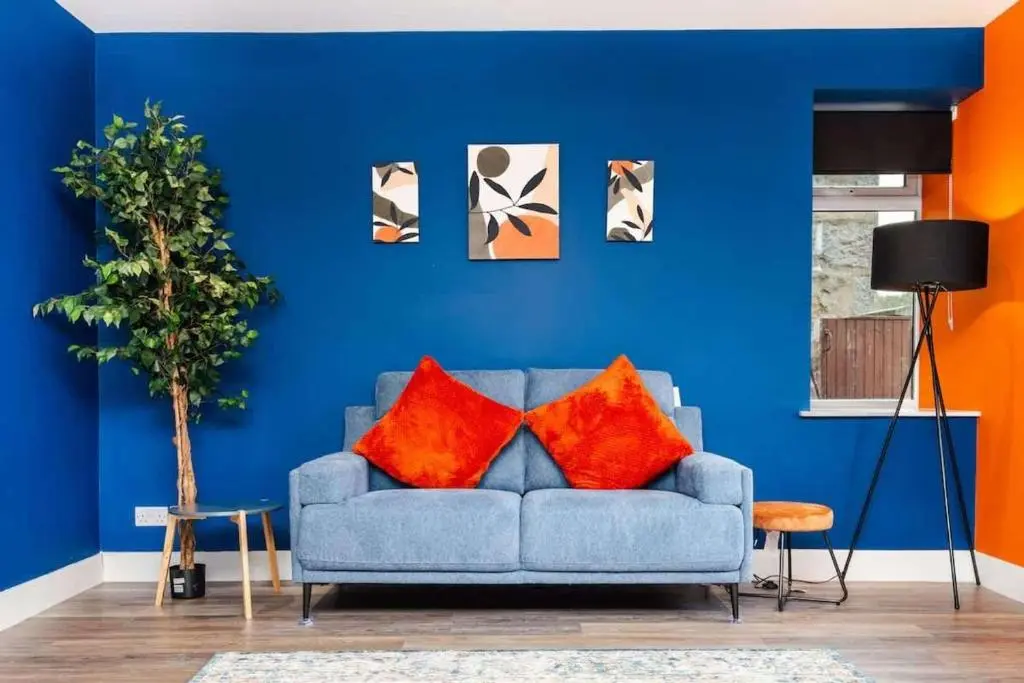 a blue living room with a blue couch with orange pillows at Airport apartment - Aberdeen - Free Parking in Aberdeen