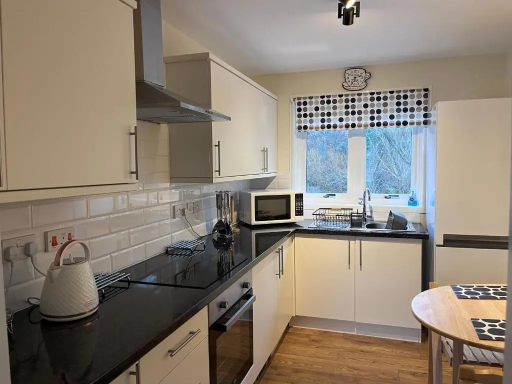 a kitchen with white cabinets and black counter tops at Millburn Court Apartment in Inverness