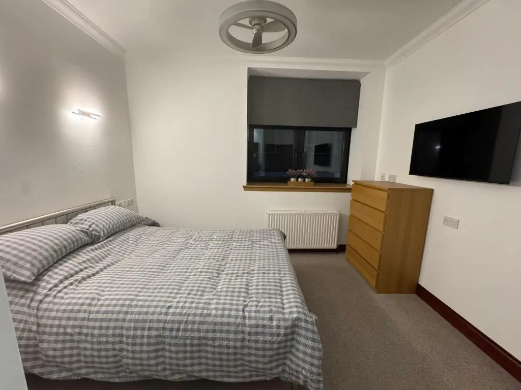 a bedroom with a bed and a dresser and a television at TSB Accommodation in Turriff