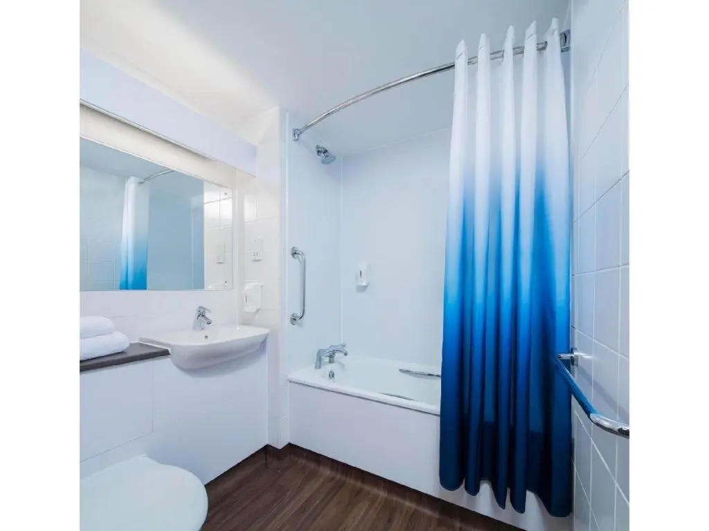 a white bathroom with a blue shower curtain and a sink at Travelodge Aberdeen Bucksburn in Aberdeen