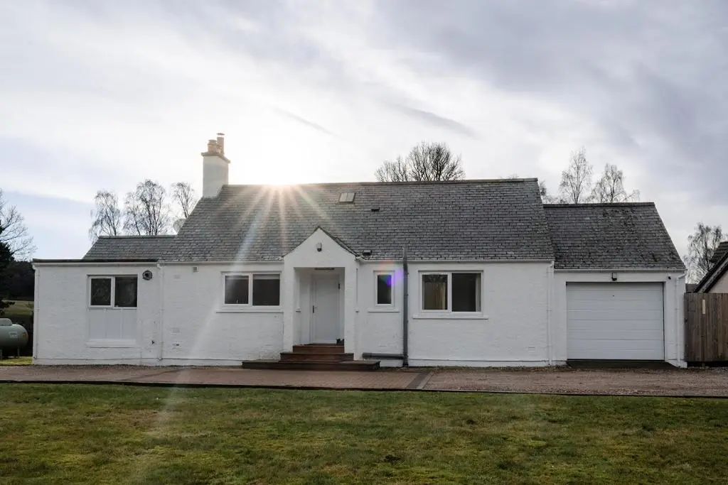 a white house with the sun shining on the roof at Inshlea - Seasgair Lodges in Insh
