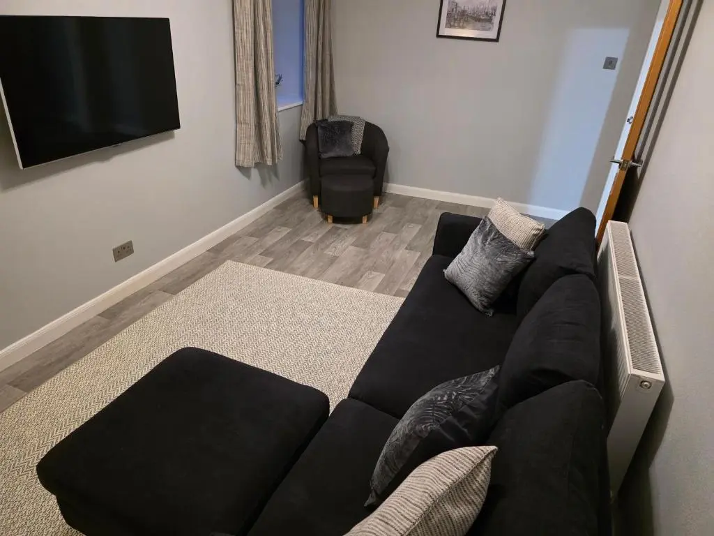 a living room with a black couch and a flat screen tv at 14 Harbour View in Wick