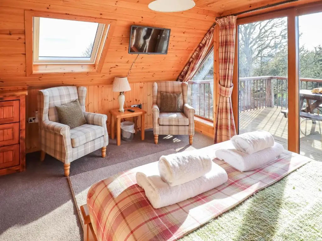 a bedroom with a bed and two chairs and a balcony at Kestrel Cottage in Rogart