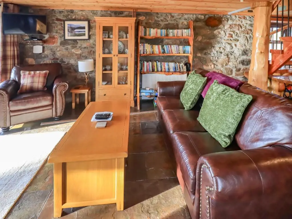 a living room with a leather couch and a table at Kestrel Cottage in Rogart
