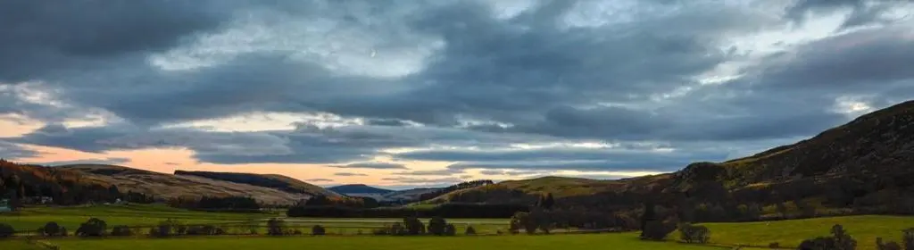 a cloudy sky over a green field with mountains at The Fortalice in Tulchan