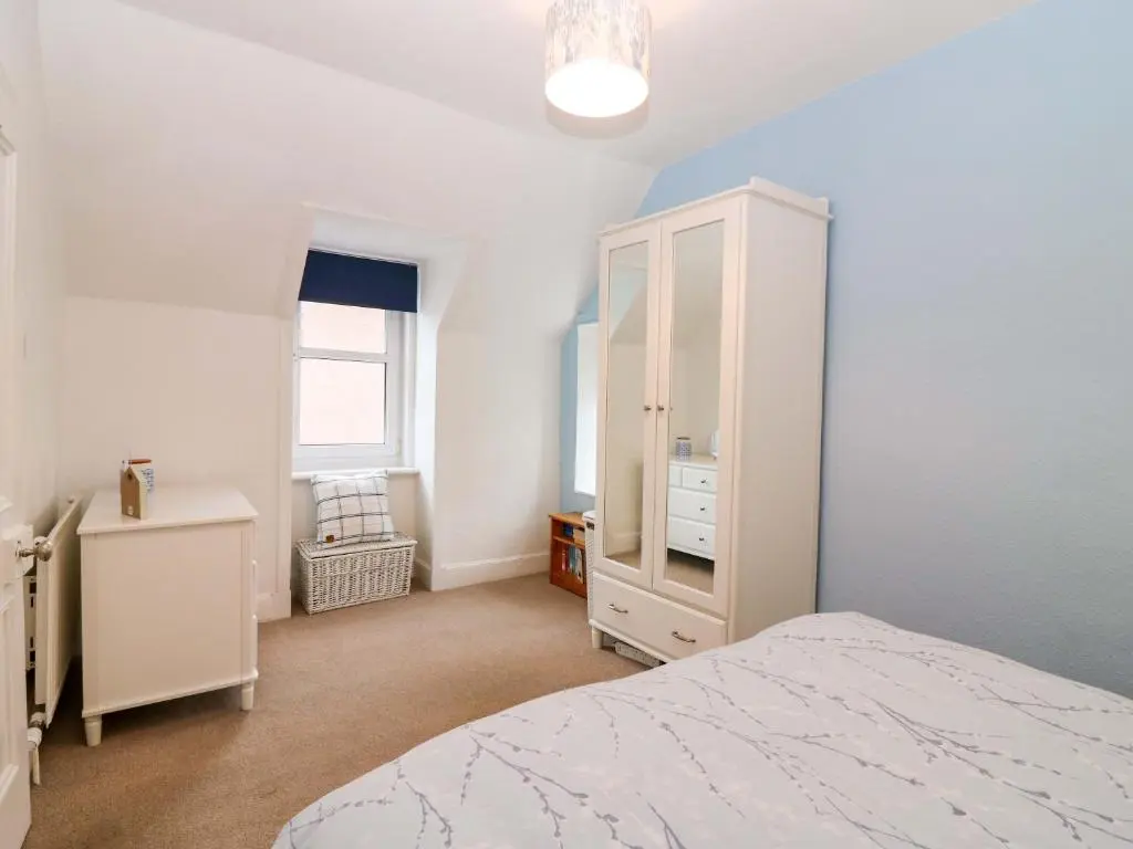 a bedroom with a white cabinet and a bed at Rose Cottage in Nairn