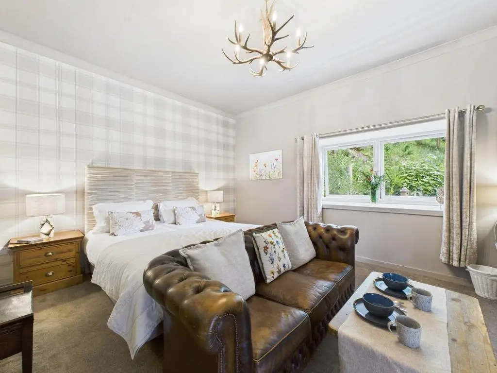 a bedroom with a bed and a leather couch at Glenshee Suite, Beechtree Cottage in Kirkmichael
