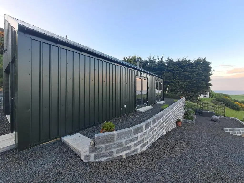 a black house with a stone retaining wall and a building at Lothmore Lookout - Sunset in Kilmote