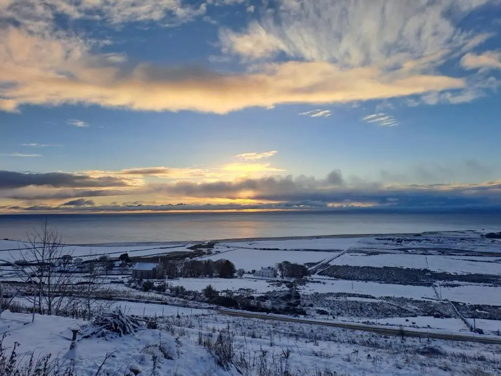 a view of a snowy field with the ocean in the background at Lothmore Lookout - Sunset in Kilmote