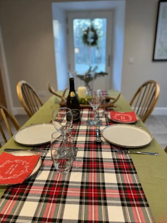 a table with a plaid table cloth and wine glasses on it at Cosy Highland Cottage in the Woods on Royal Deeside in Coldstone