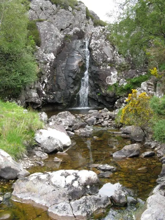 a waterfall on the side of a mountain with rocks at The Dundonnell Hotel in Dundonnell