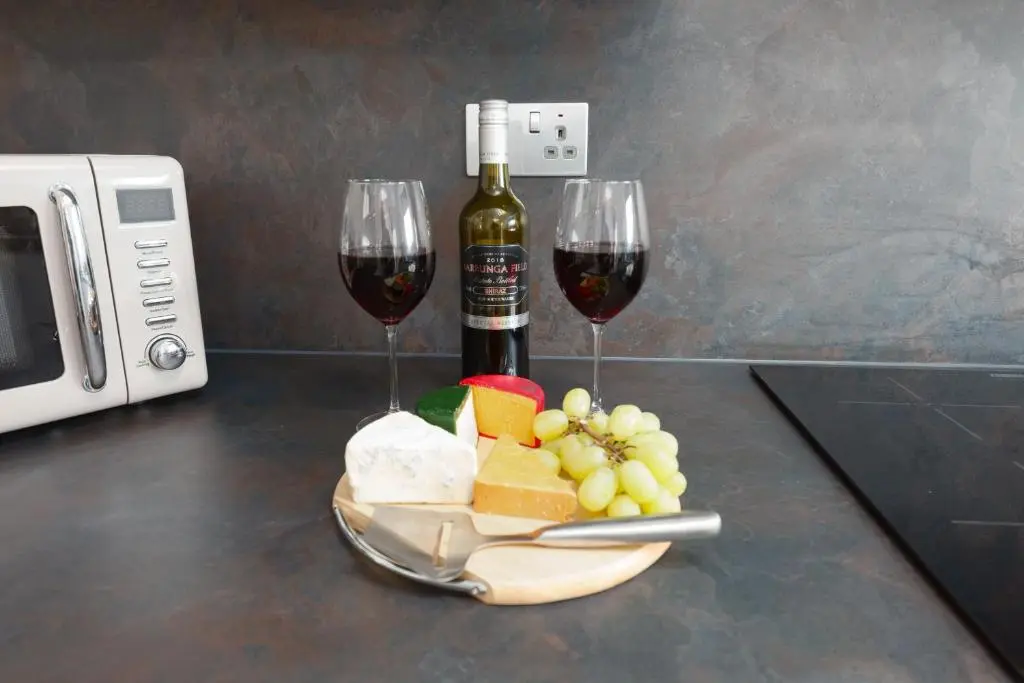 two glasses of wine and a plate of cheese and fruit at Castle Heather 2 Bedroom Holiday Home in Inshes