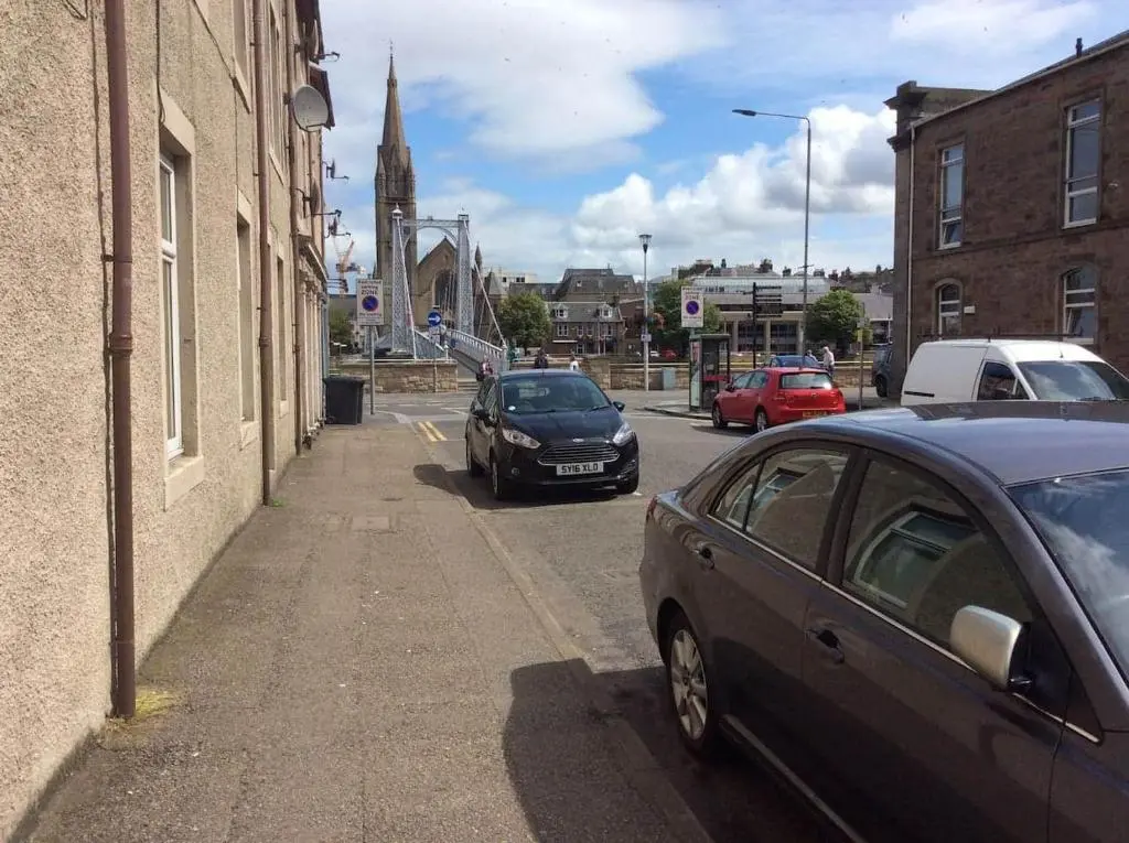 two cars parked on a city street with a church at Macdonald Apartments 9C Greig St Inverness IV3 5PT in Inverness