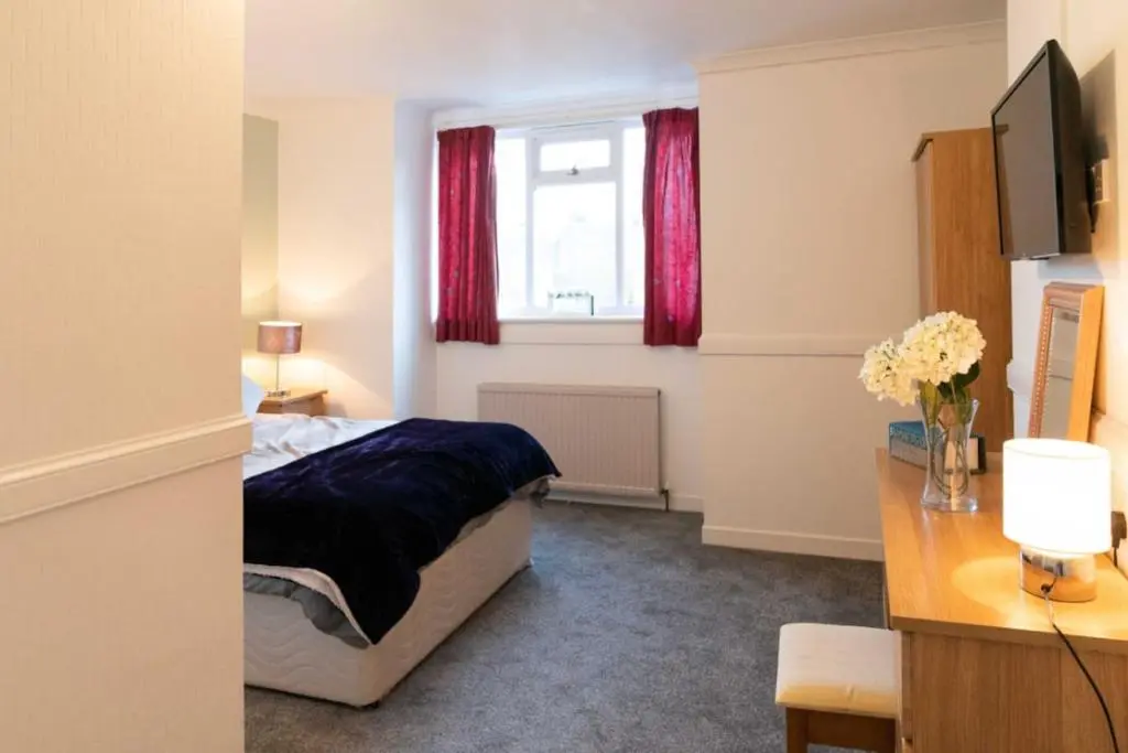 a bedroom with a bed and a window with red curtains at Dunedin House in Huntly