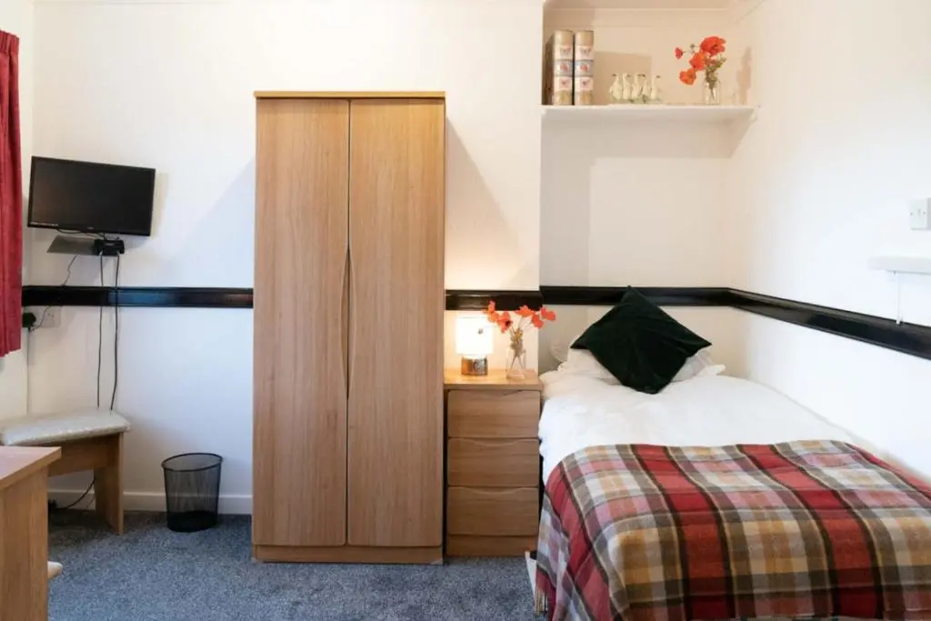 a bedroom with a bed and a wooden cabinet at Dunedin House in Huntly