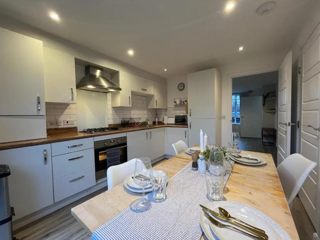 a kitchen with a wooden table and white cabinets at Skibo Place House in Inshes