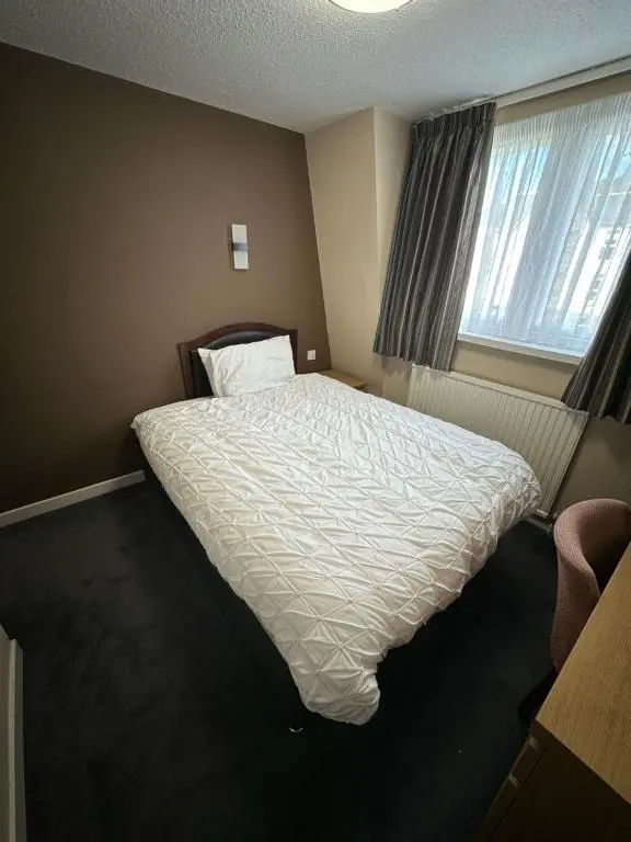 a bedroom with a bed with a white comforter and a window at Burnett Arms Hotel in Banchory