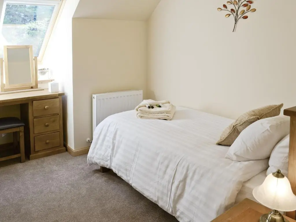 a bedroom with a white bed with a desk and a window at March Cottage in Glenrossal