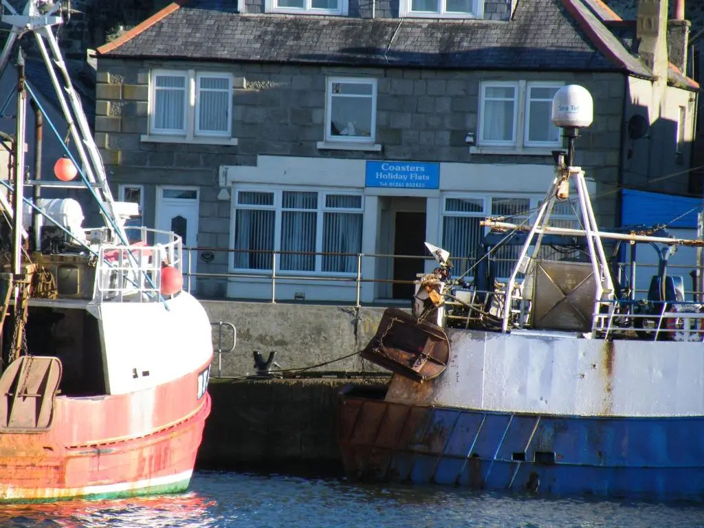 two boats docked in the water near a building at Coasters Holiday Flats in Macduff