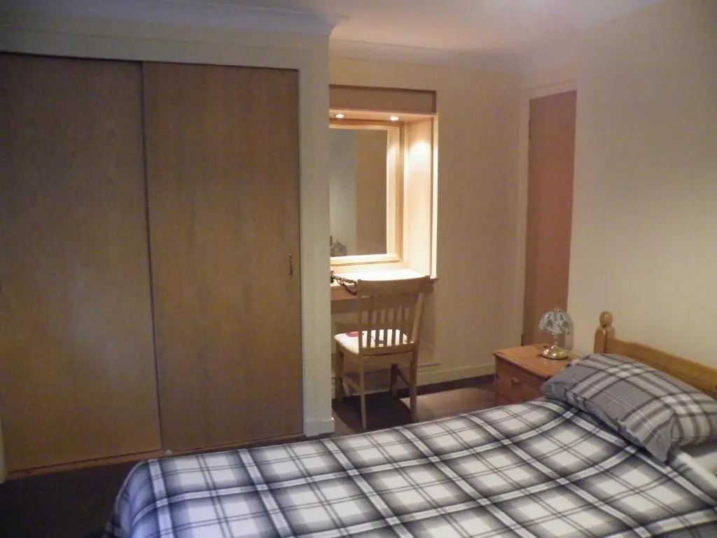 a bedroom with a bed and a desk and a chair at Coasters Holiday Flats in Macduff