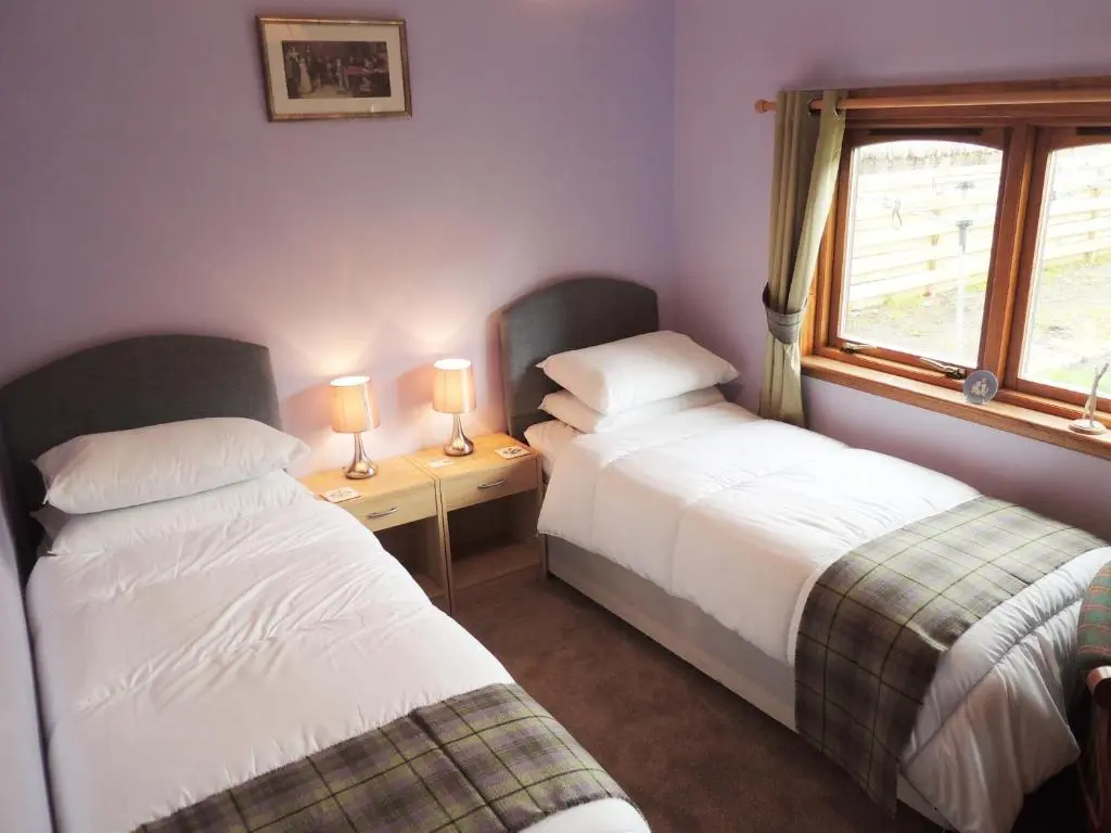 two beds in a room with a window and two lamps at Invicta House B&B in Golspie