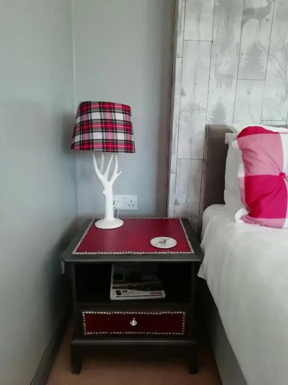 a table with a lamp on it next to a bed at Argyle Guest House in Tomintoul