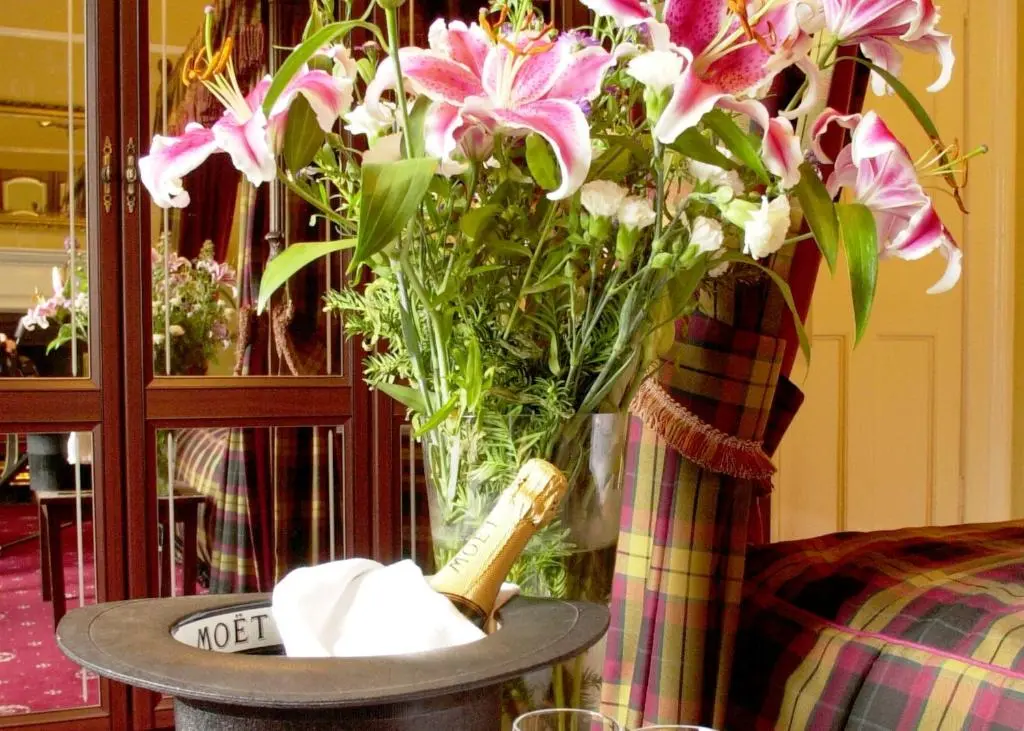 a vase of flowers on a table with a bottle of champagne at Atholl Arms in Blair Atholl