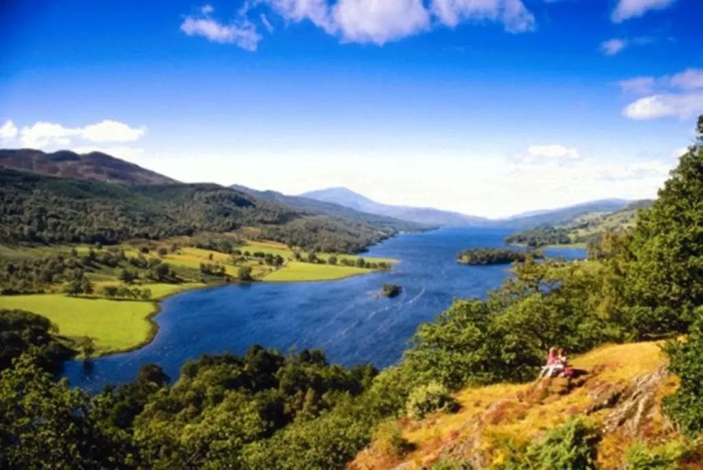 a woman sitting on a hill overlooking a river at Atholl Arms in Blair Atholl