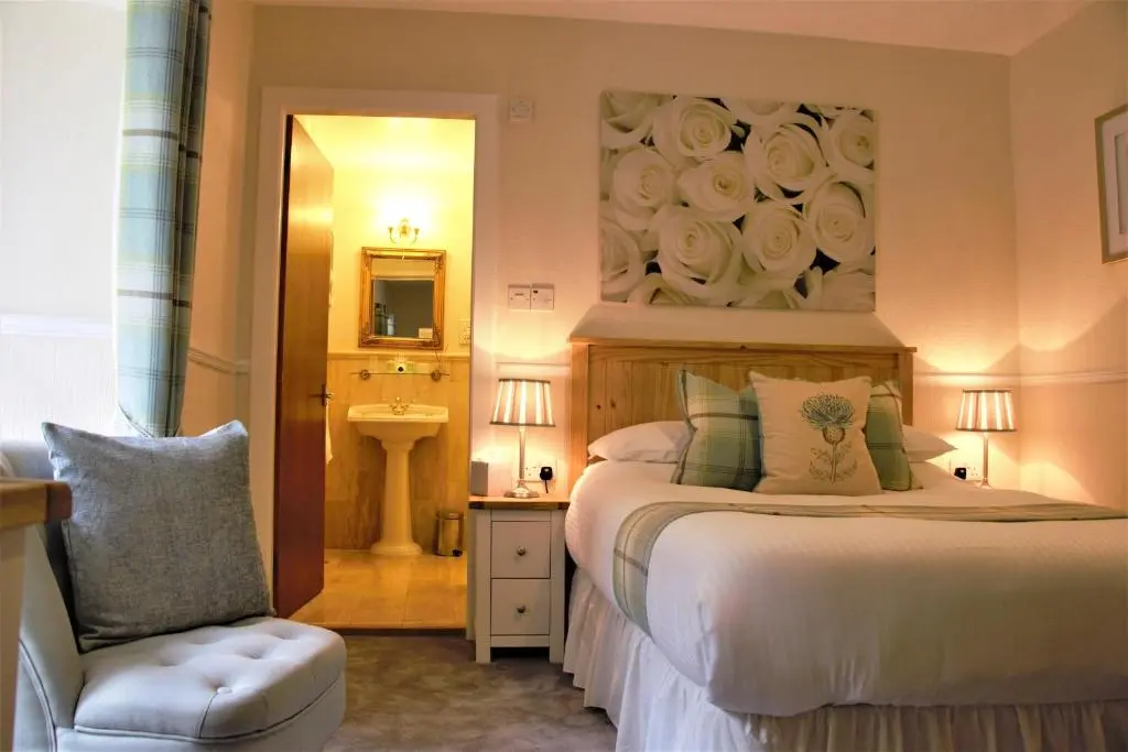 a bedroom with a bed and a chair and a mirror at Glenmoriston Arms Hotel in Invermoriston