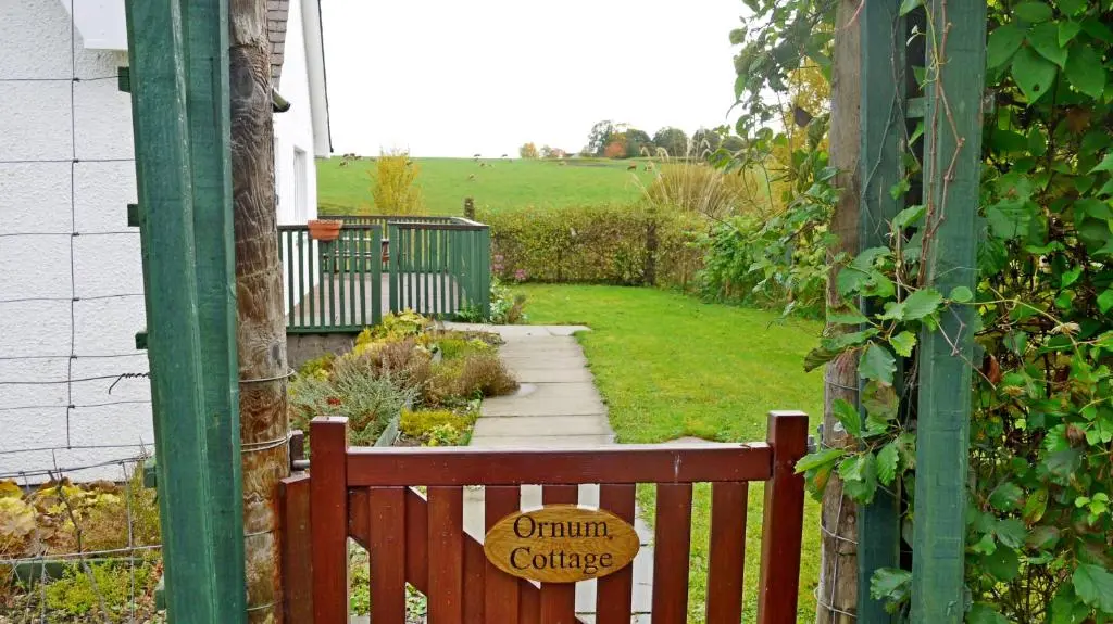 a wooden bench in a garden with a sign on it at Ornum Cottage in Beauly