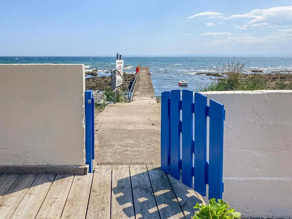 a blue gate on a beach near the ocean at Cross Tides in Hilton of Cadboll