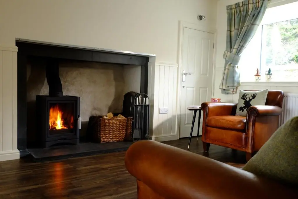 a living room with a fireplace and a couch and a chair at Otter Cottage in Inverness