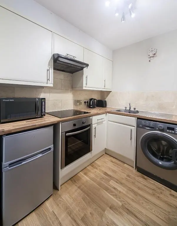 a kitchen with white cabinets and a washer and dryer at Cosy Ness Escape, 16B Ardconnel Street in Inverness