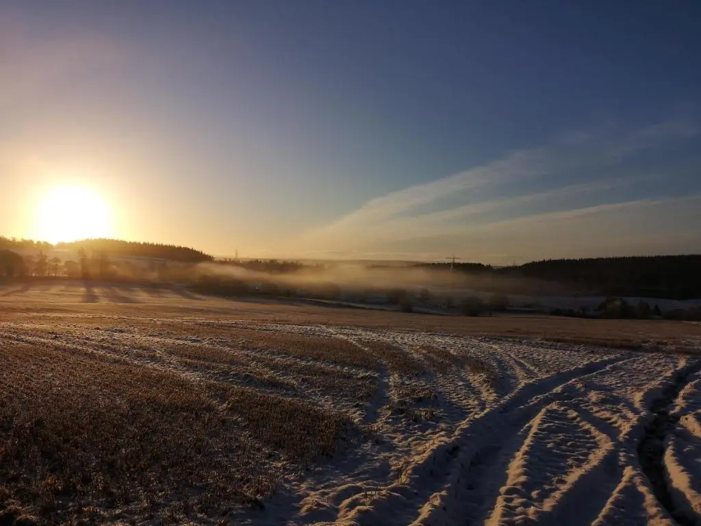a snow covered field with the sun in the background at Beechwood Lodge in Alness
