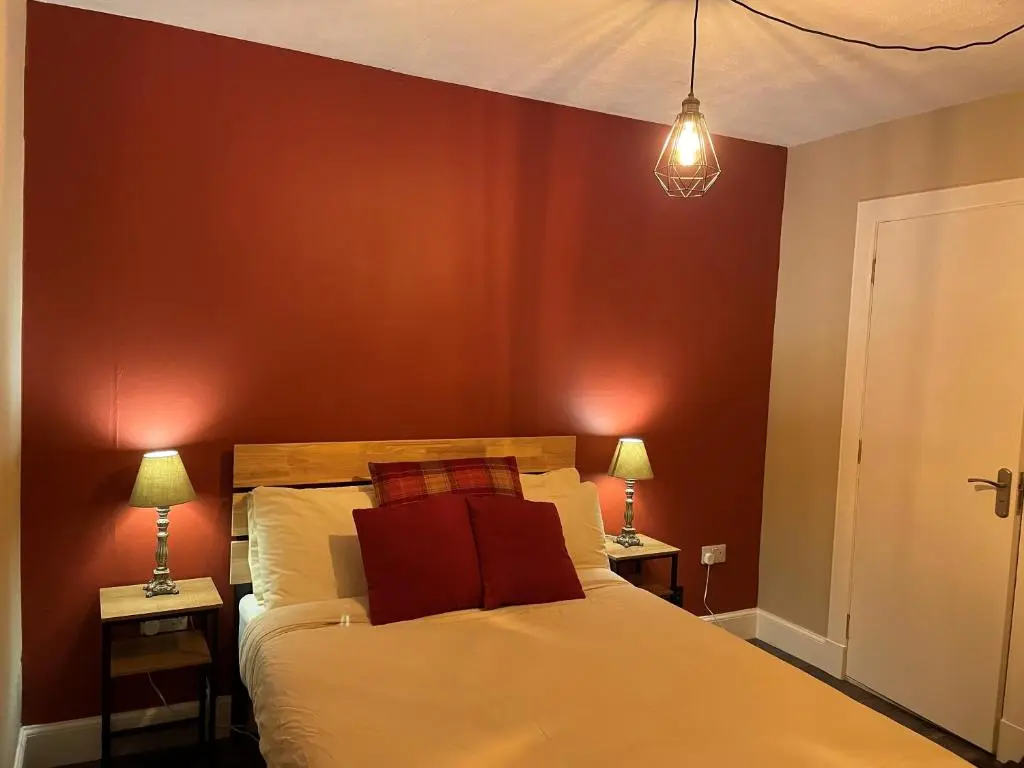 a bedroom with a bed with red walls and two lamps at Loch Ness Backpackers Lodge in Drumnadrochit