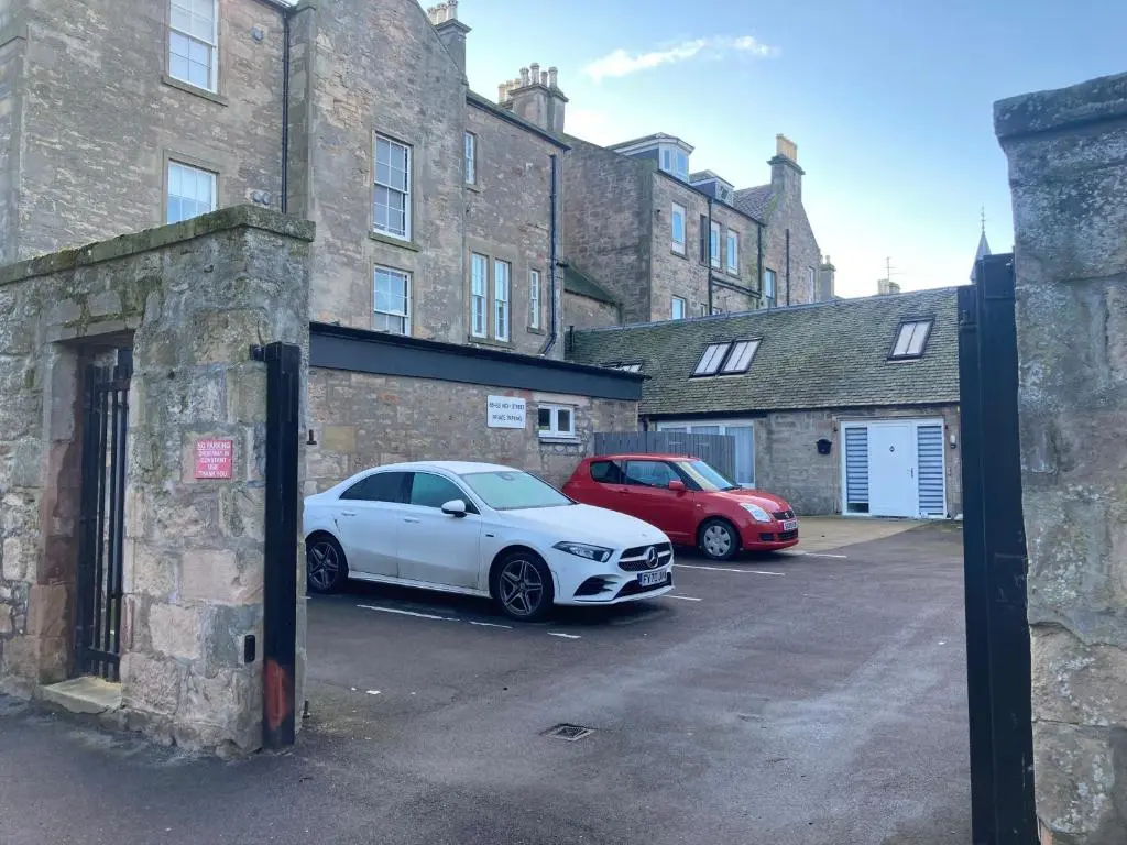 two cars parked in a parking lot next to a brick building at Luxury Apartment at Barron House in Nairn