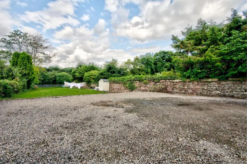 a gravel driveway with a stone wall and trees at Glasdair in Inverness