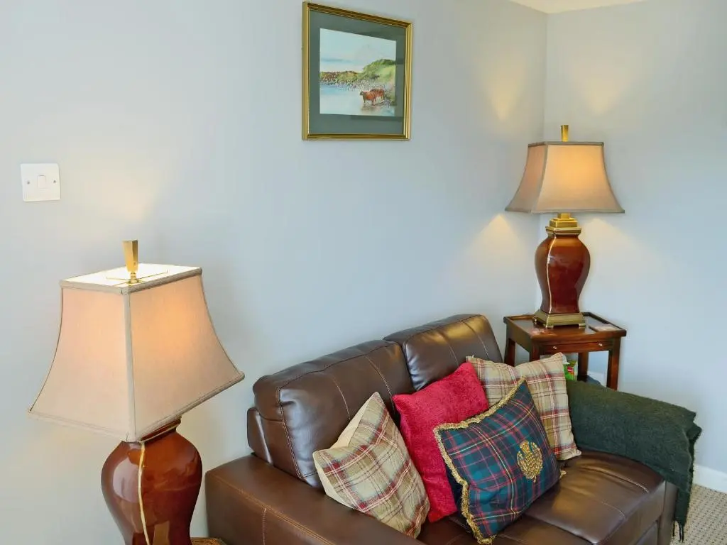 a living room with a brown leather couch and two lamps at The Wee Hoose in Achnahanat
