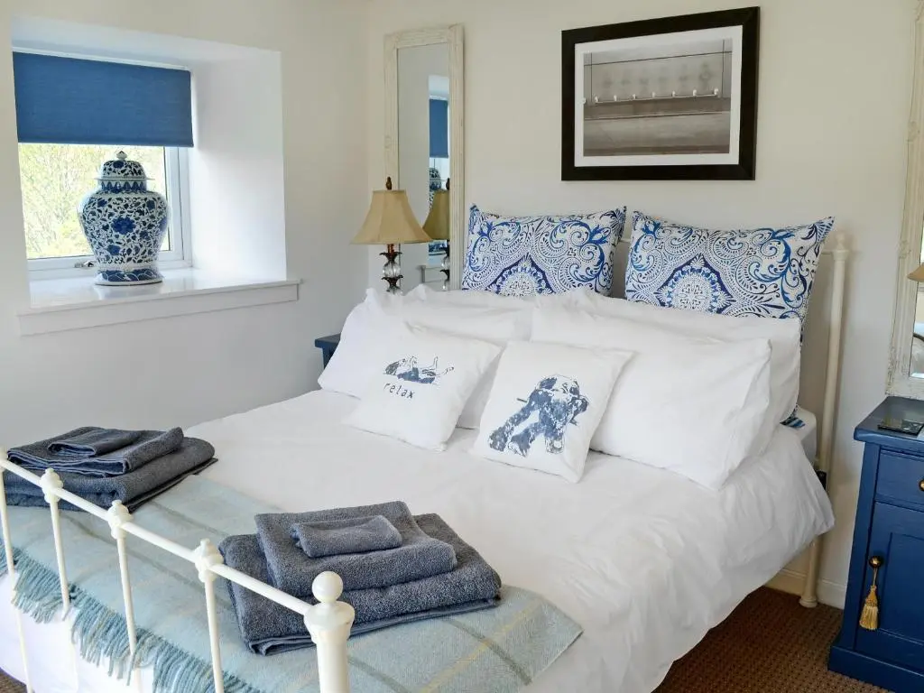 a bedroom with a white bed with blue and white pillows at The Wee Hoose in Achnahanat