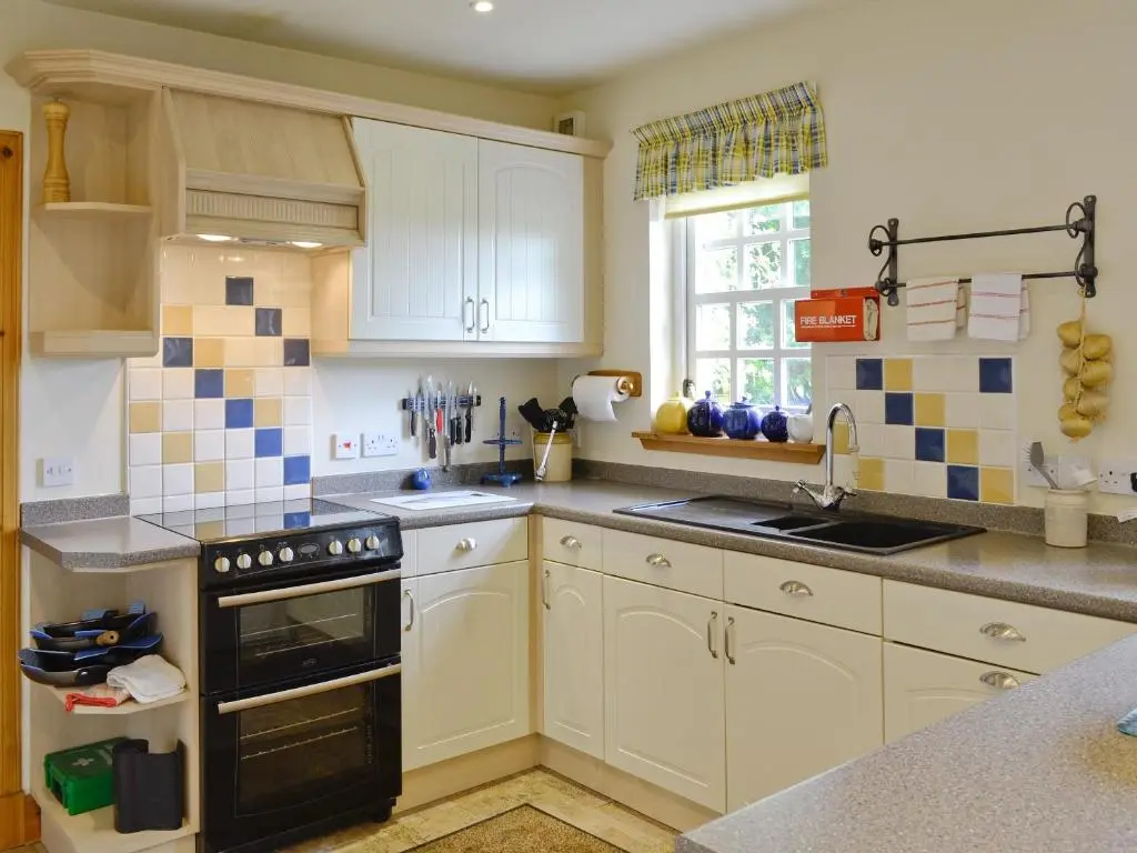 a kitchen with white cabinets and a black stove top oven at Little Blackhall Lodge in Banchory