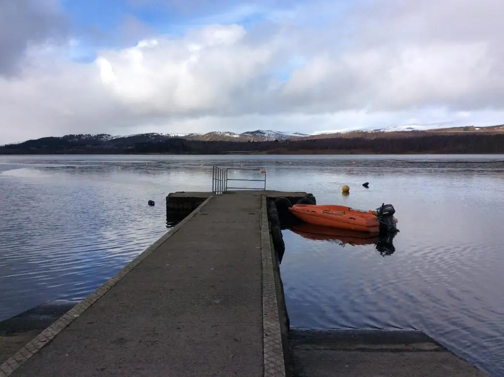 a boat sitting on the water next to a dock at Holiday House Kinveachy in Aviemore