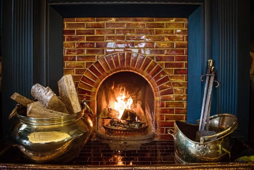a brick fireplace with a fire in it at Douneside House in Tarland