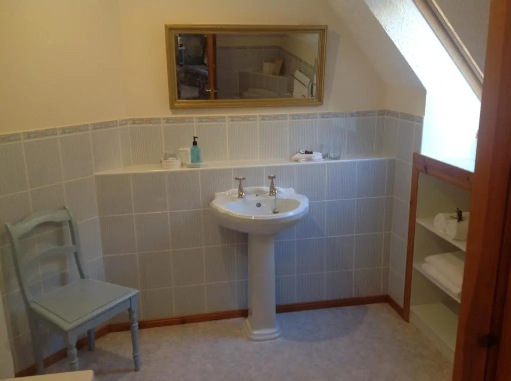 a bathroom with a sink and a mirror and a chair at Lochview Guesthouse in Contin