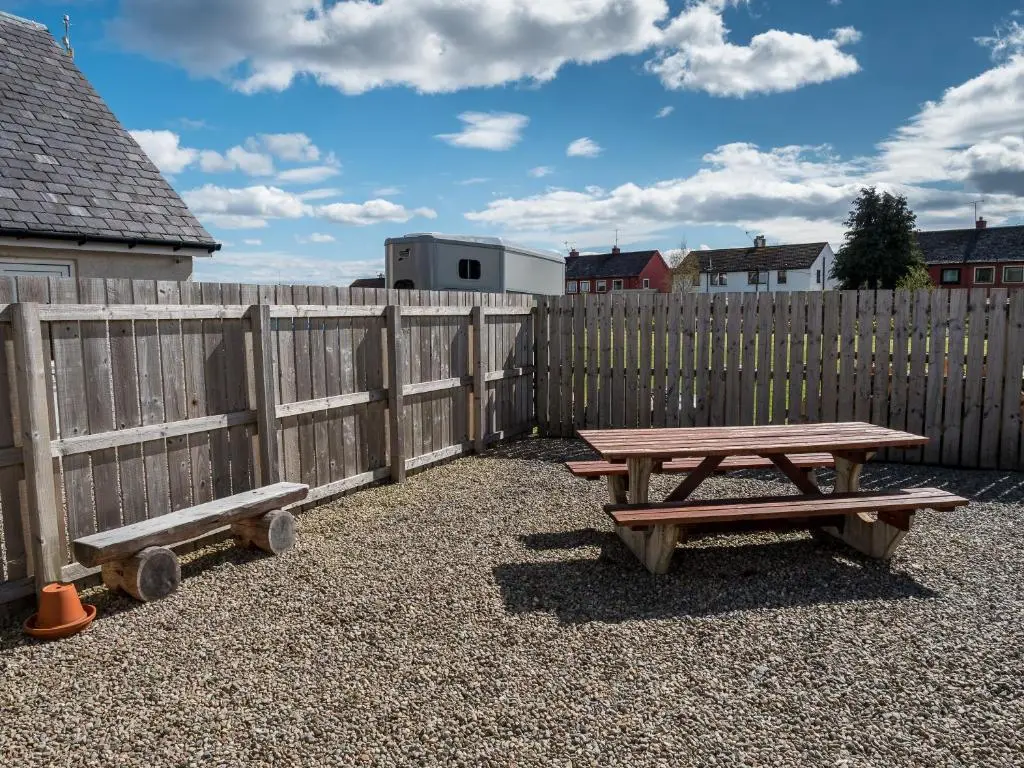a picnic table and bench in front of a fence at The Birches in Dingwall