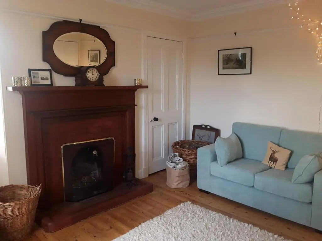 a living room with a fireplace and a blue couch at Auchencairn Cottage in Brora
