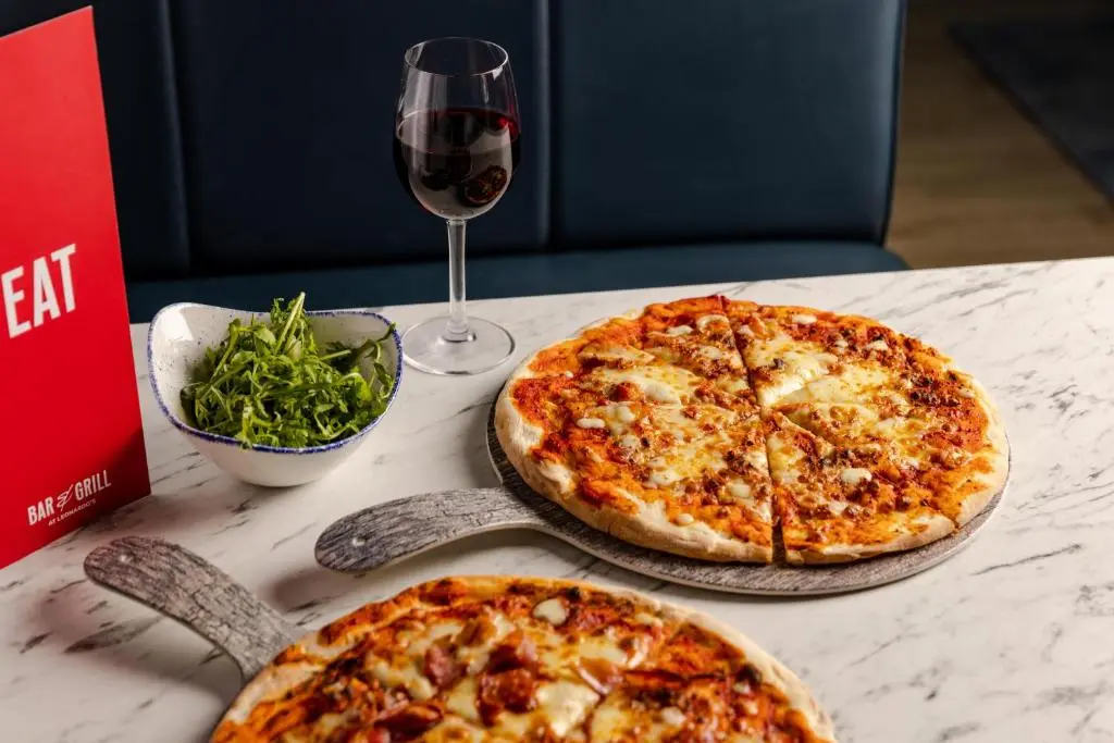 two pizzas sitting on a table with a glass of wine at Leonardo Hotel and Conference Venue Aberdeen Airport in Dyce