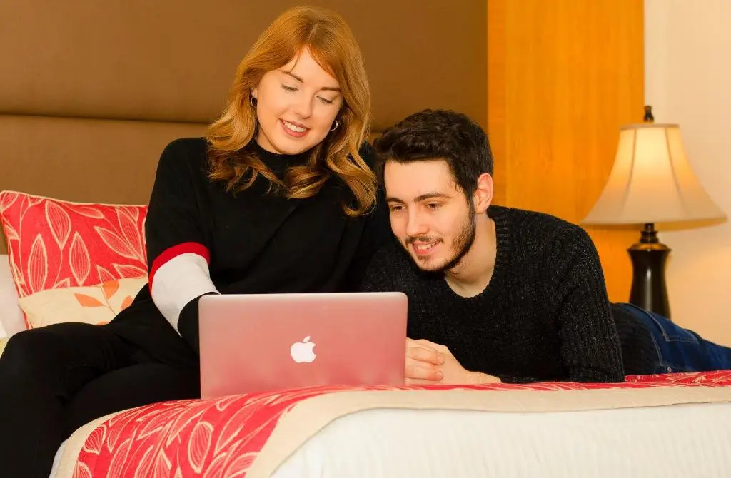 a woman and man sitting on a bed with a laptop at The Station Hotel in Portsoy