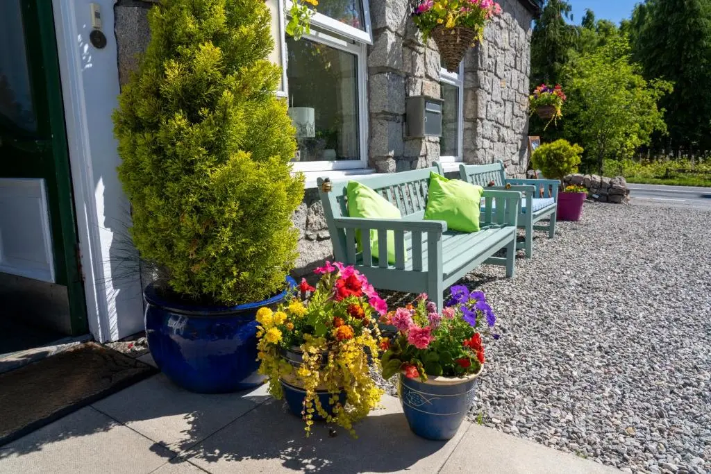 a group of benches sitting outside of a house with flowers at The Rowan Tree Country Hotel in Aviemore